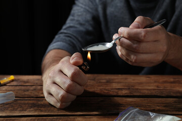 Fototapeta premium Man preparing drugs with spoon and lighter at wooden table, closeup