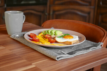 Tasty toasts with fried egg, avocado, cheese, vegetables and cup of coffee on wooden table indoors