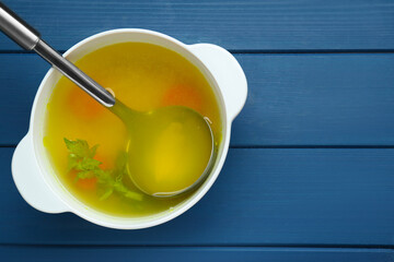 Delicious chicken bouillon with carrot and celery on blue wooden table, top view. Space for text