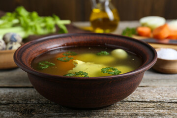 Delicious chicken bouillon with parsley, carrot and eggs on wooden table, closeup