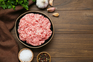 Bowl of raw fresh minced meat and ingredients on wooden table, flat lay. Space for text