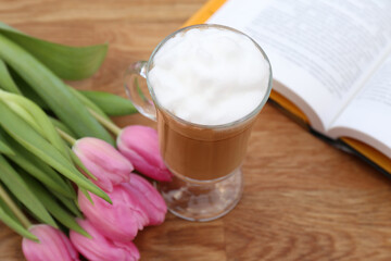 Glass of delicious cocoa, pink tulips and book on wooden table, closeup