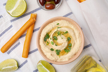 Delicious hummus with grissini sticks, lime and olives on light grey table, flat lay