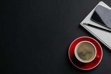 Red ceramic cup with hot aromatic coffee , notebook and smartphone on black background, flat lay. Space for text