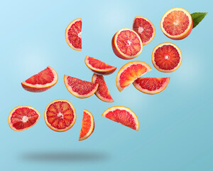 Many cut tasty Sicilian oranges falling on light blue background