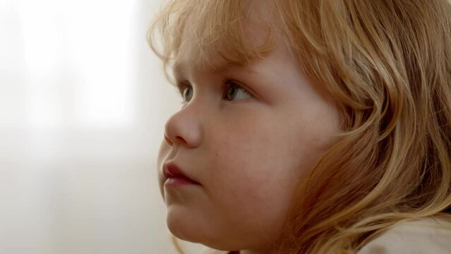 close up view of child watching TV and open her mouth. Fascinating cartoons are shown on TV for smallest people on earth. Curly-haired child girl is watching cartoons or movie intently.