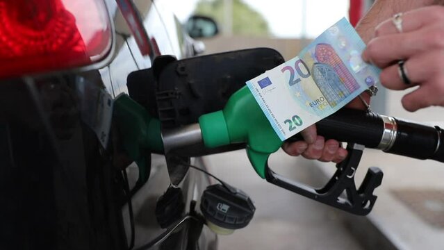 Close up of an hand refueling the car and holding a 20€ banknote, rising fuel prices.