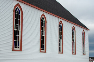 The exterior wall of a religious building with pale yellow colored narrow horizontal clapboard siding and tall Gothic-style windows with clear glass, white wooden muntins, and green wood trim. 
