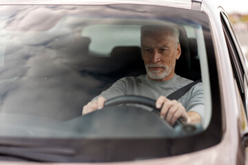 Handsome elderly man putting hands on the steering wheel, driving car. Seat bet and driving safety