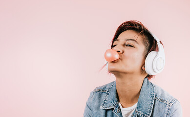 Portrait of hispanic young woman with colored hair chewing gum and headphones listening music in...