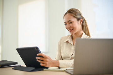 Attractive Asian businesswoman examining presentation slides on tablet, using tablet at her desk.