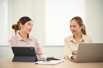 Obraz premium Two Asian female office colleagues discussing and brainstorming on their marketing project