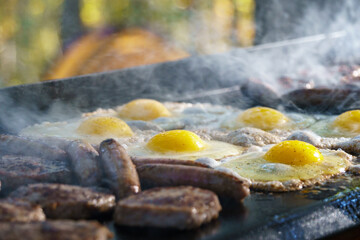 Sausages and sunny-side-up eggs cooking on an outdoor grill