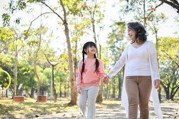 Happy Asian grandmother holding her granddaughter's hand while walking in the park together