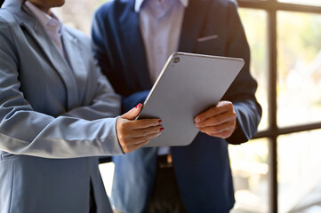 cropped image of two businesspeople stand in the office looking at tablet screen, discussing plan