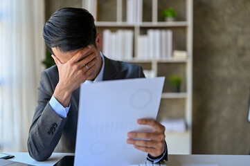 Stressed Asian businessman feels upset after looking at the financial investment outcome report