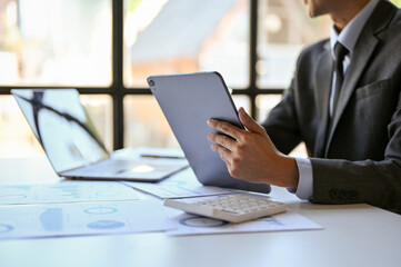 cropped image of smart Asian businessman in formal business suit sits at his desk with a tablet.