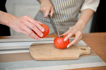 Close-up of couple preparing salad's ingredients together, cutting tomatoes on chopping board.