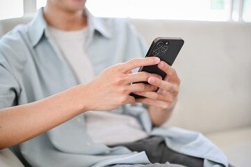 A young Asian man using his smartphone on sofa in his living room.