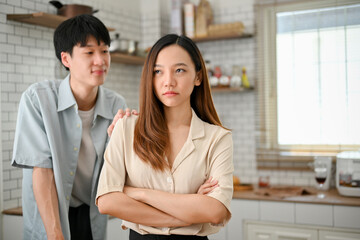 Caring Asian boyfriend is trying to comfort his angry girlfriend in the kitchen. showing care