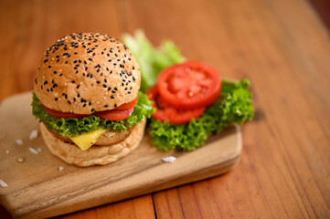 Tasty beef burger with fresh vegetables on wooden tray on wooden tabletop.
