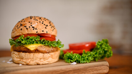 Delicious beef burger with tomato slides and lettuce on wooden tray over blurred background