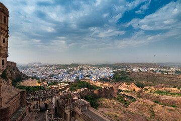 Fototapeta premium View of Mehrangarh fort with distant view of blue city Jodhpur, Rajasthan, India. Historical Fort is UNESCO world heritage site. Blue sky with white clouds in the background.