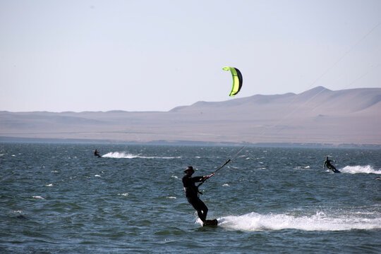 young people kitsurfing in a paracas bay of peru with blue water and drops in the air and mountains in the background-june 2020