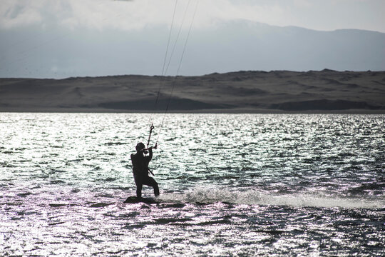 young people kitsurfing in a paracas bay of peru with blue water and drops in the air and mountains in the background-june 2020