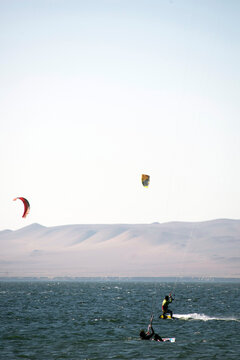 young people kitsurfing in a paracas bay of peru with blue water and drops in the air and mountains in the background-june 2020