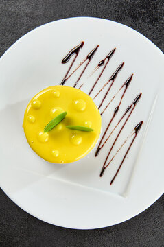 Mini Mango Cake On White Plate On Black Concrete Background. Mango Cheesecake In Minimal Style On Dark Backdrop. Light Dessert Of Cheese And Mango In Glaze Topped. Cheesecake With Tropical Flavour.