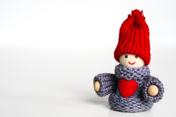 A small smiling wooden doll boy with a red knitted hat and a red heart on his chest