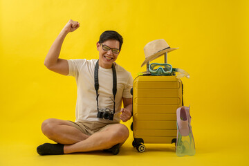Portrait of happy Asian traveler tourist man with retro camera, hat, snorkel, fins and suitcase isolated on yellow background.