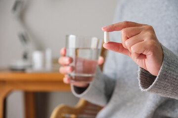 Fototapeta Closeup image of a woman holding white pills and a glass of water obraz