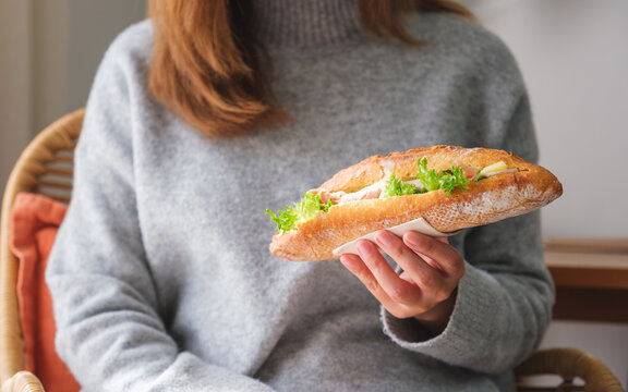 Closeup image of a woman holding a piece of french baguette sandwich at home