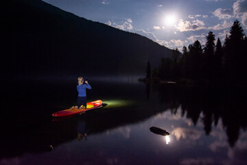 Adventurous athletic woman paddling on a paddle boards at night on an alpine lake in the Pacific Northwest.
