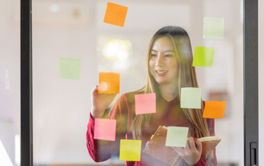 Asian businesswoman creating project plan on office wall with sticky paper notes. stylish confident manager working on business, financial and marketing planning projects. 