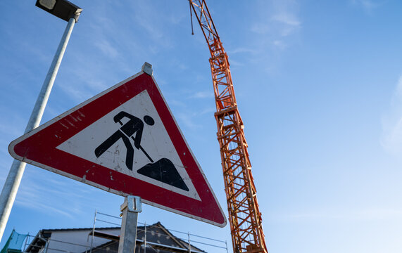 Triangular construction site sign with a construction crane in the background
