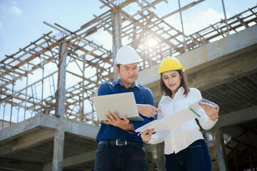 Asian Architector and engineers team with draft plan of building and tablet talking constructing site. Construction manager and engineer working on building site.