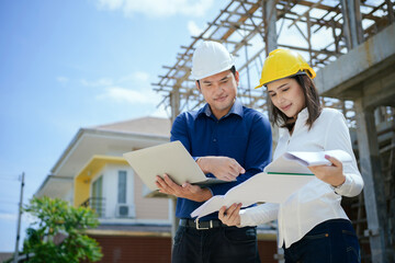 Asian Architector and engineers team with draft plan of building and tablet talking constructing site. Construction manager and engineer working on building site.