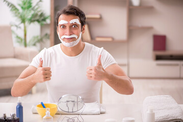 Young man shaving face at home