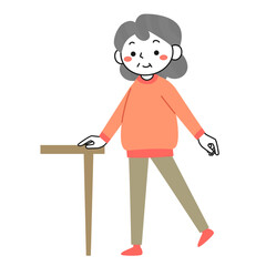 机につかまって片足立ちの運動をするシニア女性