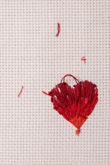 Revés de bordado de corazón con hilos rojos sobre tela cuadrillé blanca, con hilos regados
