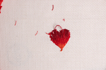 Revés de bordado de corazón con hilos rojos sobre tela cuadrillé blanca, con hilos regados