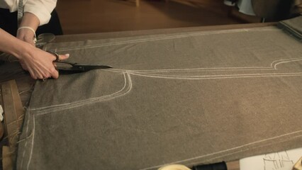 Professional female tailor cuts fabric according to sketch using scissors for sewing. Process of making clothes in luxury designer atelier or tailoring studio. Fashion and hand craft concept.
