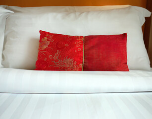 Close up A red Chinese style fabric scatter cushion, backrest pillow, placed in front of double white pillows on the hotel bed, turn down service with copy space