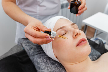 The beautician is putting essential oil on the face of women. Facial procedure for a model. Vitamins for the restoration and renewal of the face. Girl applies face serum to her face with pipette