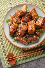 Homemade Chinese pork short ribs in sweet and sour sauce close-up in a plate on the table. Vertical top view from above