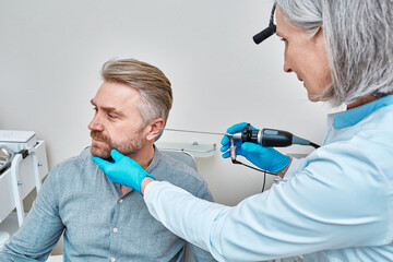 ENT doctor examining adult man's ear using endoscope at otolaryngology clinic. Ear endoscopy