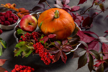 Pumpkin, apples and berries with autumn leaves on a textured table